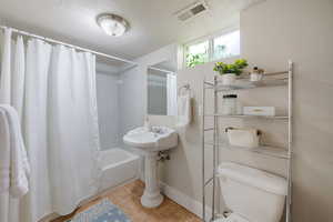 Full bathroom featuring shower / bath combo with shower curtain, a textured ceiling, and light tile patterned floors