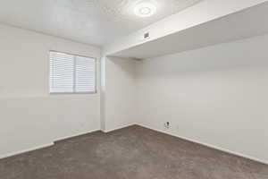 Empty room with a textured ceiling and dark carpet