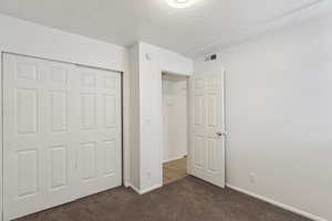 Unfurnished bedroom with a textured ceiling, carpet, a closet, and tile patterned flooring