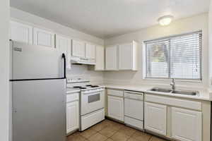 Kitchen with white appliances, a textured ceiling, white cabinets, light tile patterned floors, and light countertops