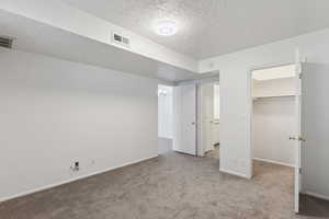 Unfurnished bedroom with carpet, a textured ceiling, and a walk in closet