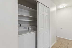 Laundry area with a textured ceiling, washer and dryer, and light tile patterned floors