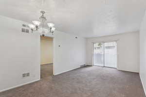 Carpeted spare room featuring a chandelier and a textured ceiling