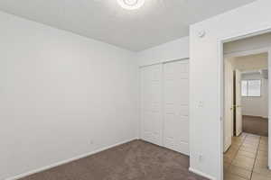 Unfurnished bedroom with light colored carpet, a textured ceiling, a closet, and light tile patterned flooring