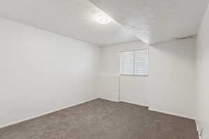 Carpeted spare room featuring a textured ceiling and baseboards