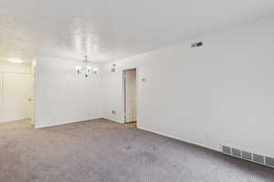 Empty room featuring a chandelier, a textured ceiling, and light colored carpet