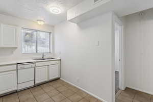 Kitchen featuring light tile patterned floors, white dishwasher, white cabinetry, a textured ceiling, and light countertops