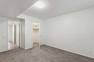 Unfurnished bedroom with carpet flooring, a textured ceiling, a spacious closet, and tile patterned flooring