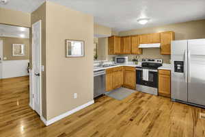 Kitchen featuring stainless steel appliances, light countertops, light wood-type flooring, under cabinet range hood, and a textured ceiling