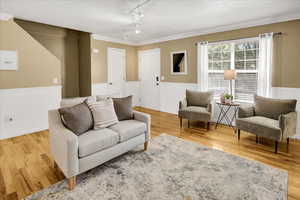 Living room with ornamental molding, wood finished floors, and a wainscoted wall