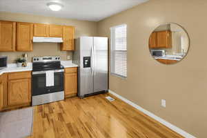 Kitchen with stainless steel appliances, light wood finished floors, light countertops, under cabinet range hood, and brown cabinets