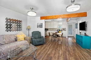 Living area featuring dark wood-style flooring, beamed ceiling, and a textured ceiling