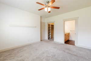 Unfurnished bedroom with dark carpet, a spacious closet, ceiling fan, and connected bathroom