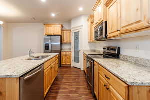 Kitchen with appliances with stainless steel finishes, light brown cabinetry, recessed lighting, dark wood-style floors, and a center island with sink
