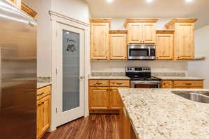 Kitchen with stainless steel appliances, light brown cabinetry, dark wood-style floors, light stone counters, and recessed lighting