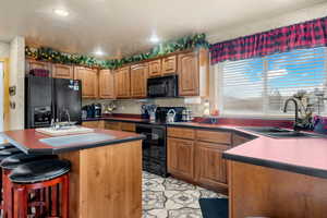 Kitchen featuring dark countertops, black appliances, brown cabinets, a breakfast bar area, and recessed lighting