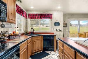 Kitchen featuring black appliances, dark countertops, brown cabinetry, and recessed lighting