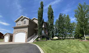 View of front of home featuring a front yard, asphalt driveway, stone siding, and a garage