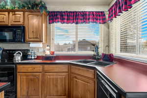 Kitchen featuring black appliances, dark countertops, healthy amount of natural light, and brown cabinets