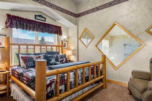 Carpeted bedroom with wallpapered walls and lofted ceiling