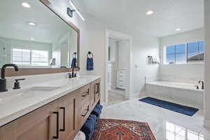 Bathroom with a bath, double vanity, a textured ceiling, and recessed lighting