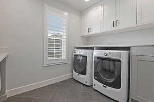Washroom featuring separate washer and dryer, cabinet space, and dark tile patterned floors