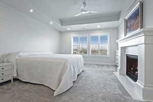 Carpeted bedroom with recessed lighting, a fireplace with flush hearth, a raised ceiling, and ceiling fan