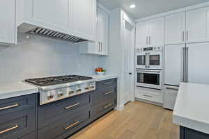 Kitchen with built in fridge, light wood-style floors, white cabinets, double oven, and stainless steel gas stovetop
