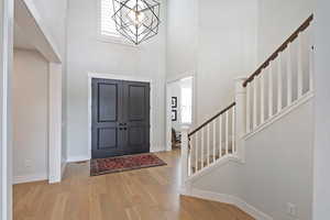 Entrance foyer featuring stairs, light wood-style floors, a towering ceiling, and a chandelier