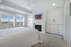 Bedroom featuring recessed lighting, light carpet, a warm lit fireplace, ceiling fan, and a raised ceiling