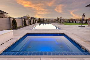 Pool at dusk with an in-ground hot tub, a residential view, and a patio area