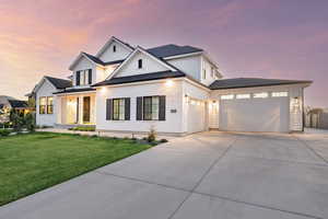 Modern farmhouse featuring driveway, an attached garage, a front lawn, board and batten siding, and a shingled roof