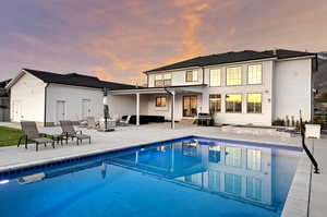 Back of house at dusk featuring a patio, a fire pit, and an outdoor pool