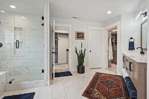 Full bath featuring a spacious closet, marble finish floors, vanity, a shower stall, and recessed lighting