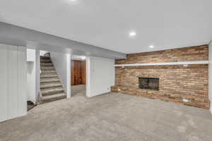 Finished basement featuring carpet, stairs, a fireplace, brick wall, and recessed lighting