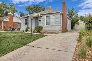 View of front of property featuring an outbuilding, a front lawn, a chimney, concrete driveway, and a detached garage