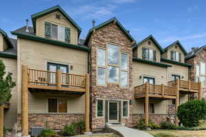 Rear view of property featuring a balcony, stone siding, and a shingled roof