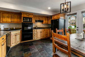 Kitchen featuring black appliances, dark countertops, dark stone finish floors, recessed lighting, and brown cabinets