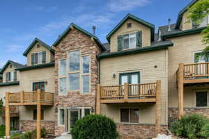 Back of house with a balcony, stone siding, roof with shingles, and french doors