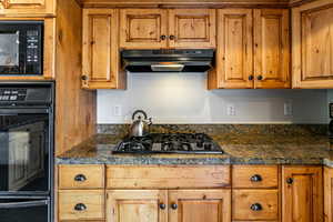 Kitchen with black appliances, dark countertops, under cabinet range hood, and brown cabinets