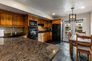 Kitchen with recessed lighting, stone tile flooring, black appliances, brown cabinetry, and a chandelier