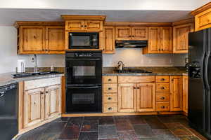 Kitchen featuring black appliances, ventilation hood, dark stone finish flooring, and brown cabinets