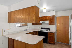Kitchen featuring electric stove, brown cabinets, a peninsula, light countertops, and under cabinet range hood