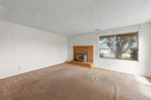 Unfurnished living room featuring a textured ceiling, carpet flooring, and a fireplace