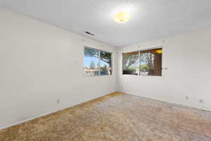 Carpeted empty room with a textured ceiling and baseboards