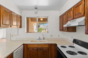 Kitchen featuring white appliances, under cabinet range hood, light countertops, and brown cabinetry