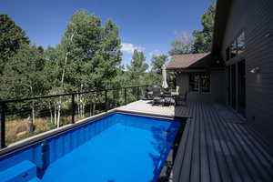 View of swimming pool with outdoor dining space, a deck, and view of wooded area