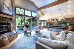 Living area featuring beamed ceiling, a stone fireplace, light wood-style flooring, high vaulted ceiling, and a chandelier