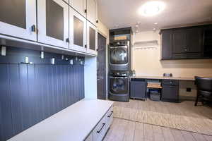 Laundry room with stacked washer / drying machine, a textured ceiling, an office area, and wood tiled floors