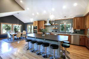 Kitchen featuring a center island, stainless steel appliances, decorative backsplash, wall chimney range hood, and brown cabinetry